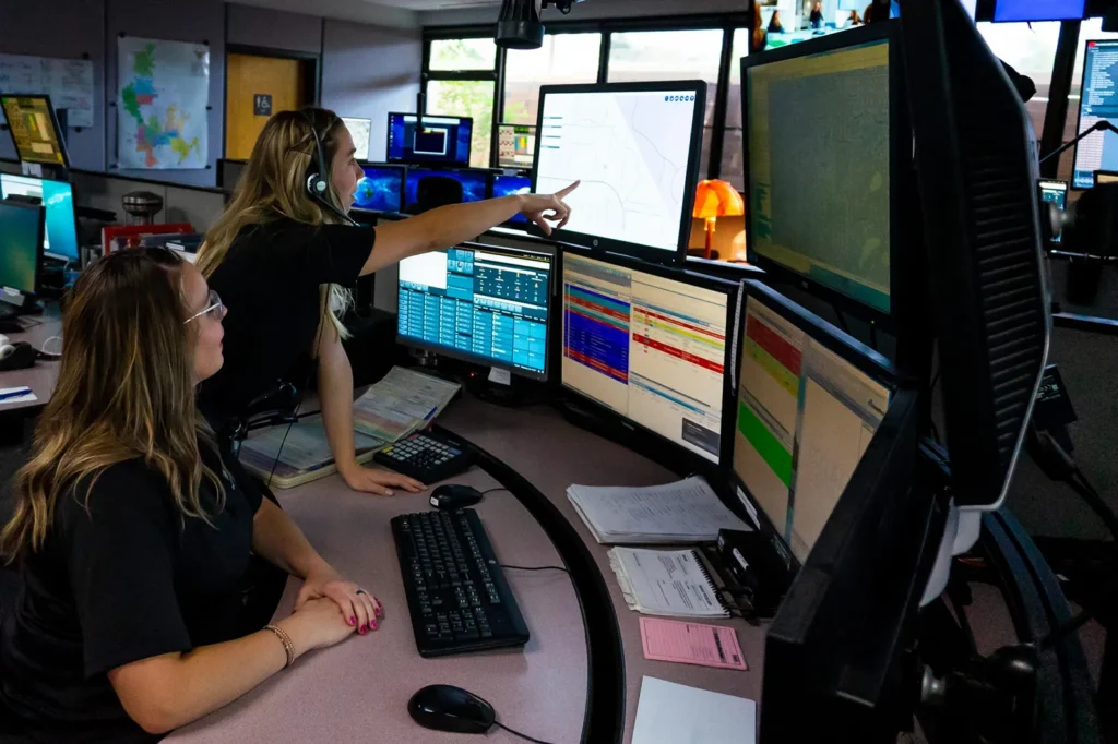 Prescott Regional Communications Center. Woman pointing at monitors as another woman looks on.