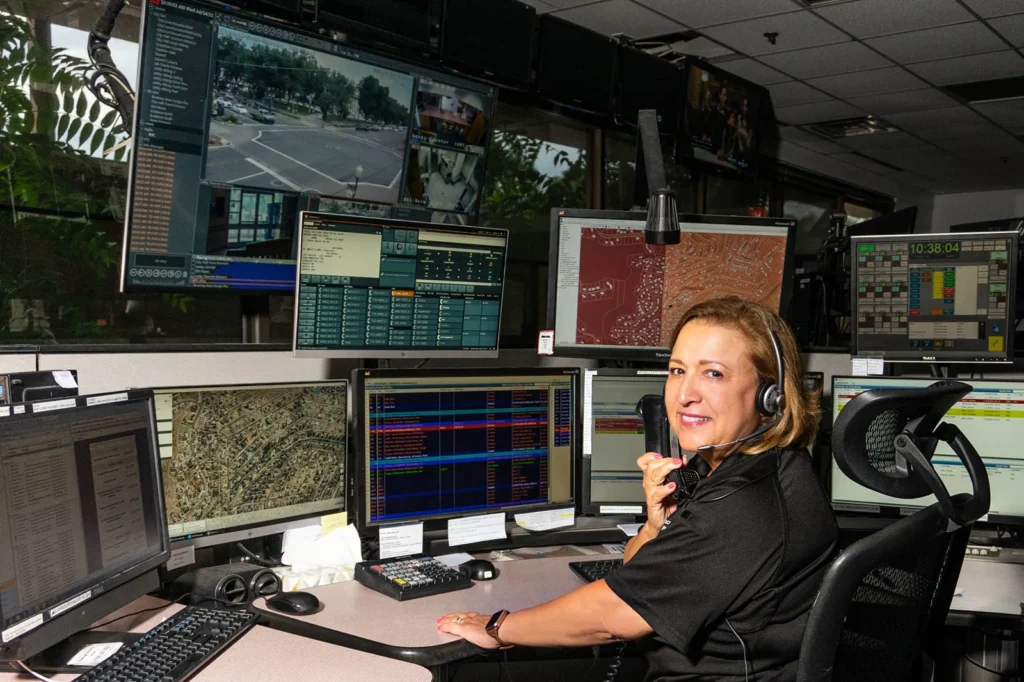 Prescott Regional Communications Center. Woman smiling at camera with headset on and lots of monitors.