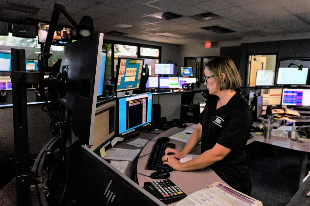 Prescott Regional Communications Center. Woman smiling at camera with headset on and typing on keyboard in the communications center.